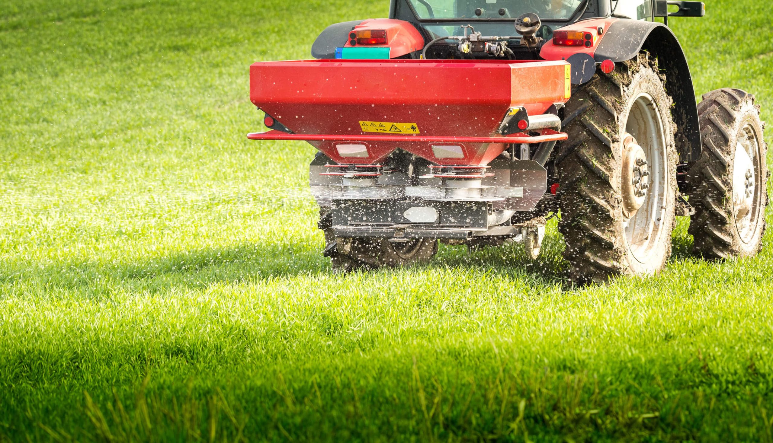 A tractor-mounted fertilizer spreader applying nutrients to a lush green lawn