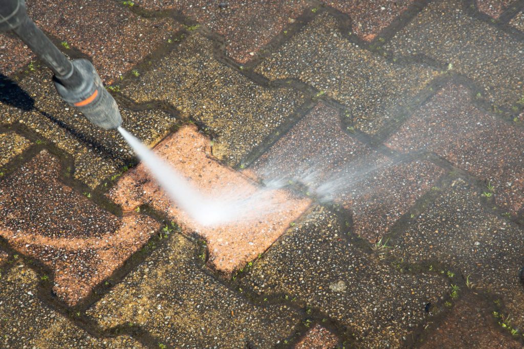 High-pressure power washing blasting dirt and grime off paver bricks on an outdoor surface