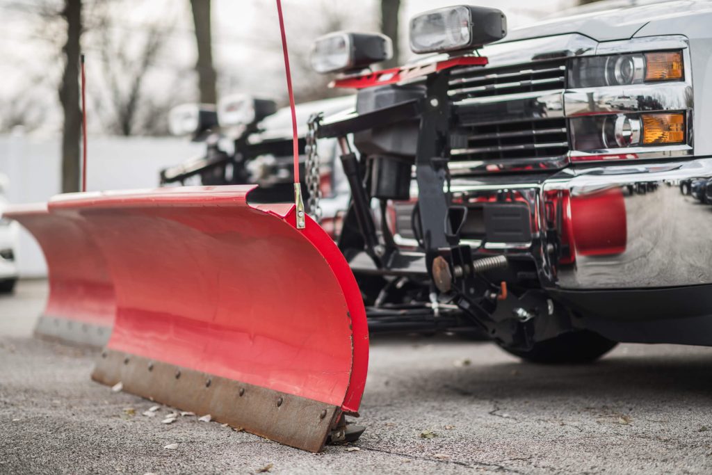 A red snow plow attached to a vehicle clearing snow during winter conditions.